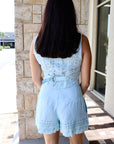 Woman wearing a light blue romper standing in front of a stone wall.