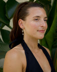 Woman wearing a black dress and xoxo earrings with plants in the background
