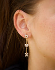 Close-up of a person wearing gold earrings with heart and x and o designs.