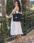 Woman in a white dress holding a black patterned handbag on a sidewalk.
