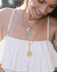 Woman wearing a white dress and multiple necklaces with pendants.
