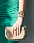 Person wearing a green dress with bracelet stack holding a gold clutch with a plain background
