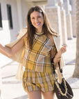 Woman in a yellow plaid outfit holding a black handbag outdoors.