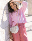 Woman in pink outfit with white handbag leaning against a wall.