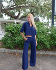Woman in a blue outfit standing outdoors with greenery in the background, full body