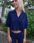 Woman wearing a blue outfit standing outdoors with greenery in the background