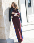 model wearing burgundy pants with a blue stripe wearing leather jacket and a burgundy sweater with white details with a shopping center as the background