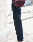 A person outdoors wearing dark wide-leg jeans and metallic silver pointed-toe heels, holding a burgundy woven pouch bag.