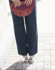 A person outdoors wearing dark wide-leg pants, a dark top, and metallic silver heeled sandals, holding a burgundy woven clutch bag.