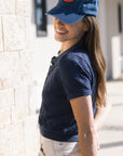Woman wearing a blue cap and navy shirt standing against a light-colored wall.