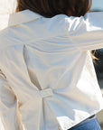 A close-up back view of a person wearing a white button-front shirt with a unique split back detail and blue jeans.