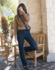 A woman posing outdoors in a brown and beige diamond-patterned knit sweater, dark blue jeans, and brown shoes, carrying a small black crossbody bag.