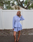 Woman wearing a light blue set standing in front of a white fence with trees in the background