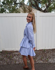 Young girl in a light blue set standing outdoors with a white fence and trees in the background, side view