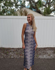 Woman in a zebra-striped dress standing outdoors with a white fence and trees in the background.