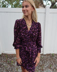 Woman wearing a purple patterned dress standing in front of a white fence, close up front