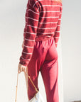 A woman wearing a fuzzy red and white striped long-sleeve sweater and matching red pants, holding a white handbag with a gold strap, standing against a white wall.