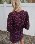 Person wearing a purple and black patterned dress with a white fence and trees in the background. close up back