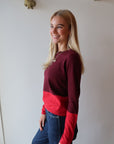 Woman wearing a red and maroon sweater standing against a white wall, side view