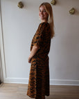 Person wearing a tiger print outfit standing in a room with white walls and wooden flooring, side view