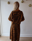 Person wearing a tiger-striped outfit standing against a white wall, back