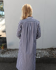 Person wearing a grey and white striped shirt standing on a sidewalk. back