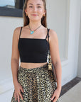 Woman wearing a black top and leopard print skirt standing outdoors.