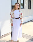 Woman in a white outfit with a floral cardigan standing in front of a white building.
