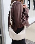 Person wearing a brown top with an ivory handbag on a neutral background