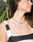 Woman wearing a gold necklace and orange earrings with a blurred plant background