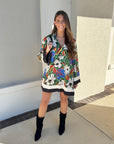 Woman wearing a colorful floral dress with black boots standing in front of a building.
