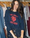A woman smiling while wearing a navy blue crewneck sweatshirt with a red 'THE GREAT PANTHERS' graphic on the front, standing in front of a clothing rack.