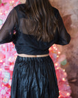 Person wearing a black outfit with sheer sleeves in front of a pink decorative background, back view