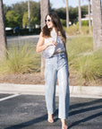 Woman in a sequin top and light blue jeans standing in a parking lot with palm trees in the background.