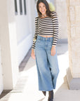 Woman wearing a striped shirt and wide-leg jeans standing outdoors.