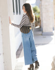 Woman wearing a striped sweater and blue jeans standing outdoors, back