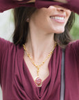 Woman wearing a gold necklace with a red pendant and Natia Cowl Neck Top smiling outdoors.