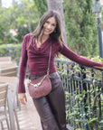 Woman in burgundy top and brown pants with a red and raisin checkered bag outdoors.