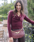 Woman wearing a burgundy top and patterned bag outdoors with greenery in the background