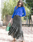 Woman wearing a blue top and black polka dot skirt with a green handbag outdoors.