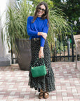 Woman in a blue sweater and polka dot skirt holding a green handbag outdoors.