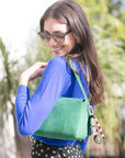 Woman wearing a blue sweater and green bag with Cameo Fob outdoors with blurred background