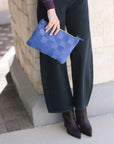 Person wearing black jeans, Mikki Block Heel Boot, holding a blue checkered clutch against a stone wall.