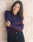 Woman wearing a striped shirt and jeans standing against a stone wall, arms crossed