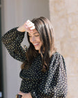 Woman wearing a black polka dot top with long sleeves, standing outdoors, front/side