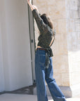 Woman in a polka dot blouse and blue jeans standing against a stone wall, back/side view