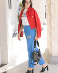 Woman wearing a red jacket, white t-shirt, blue jeans, and black high-heeled shoes, holding a black handbag, full body