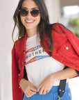 Woman wearing a red jacket, white t-shirt with text, and blue pants outdoors.