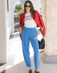 Woman wearing a red jacket, white graphic t-shirt, blue pants, and black shoes outdoors, full body view