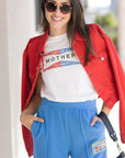 Woman wearing a red jacket, white graphic t-shirt, and blue pants with a blurred background